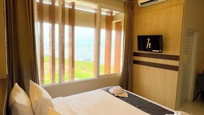 Une chambre d’hôtel avec un grand lit, un téléviseur fixé au mur et une vue sur la mer par la fenêtre.