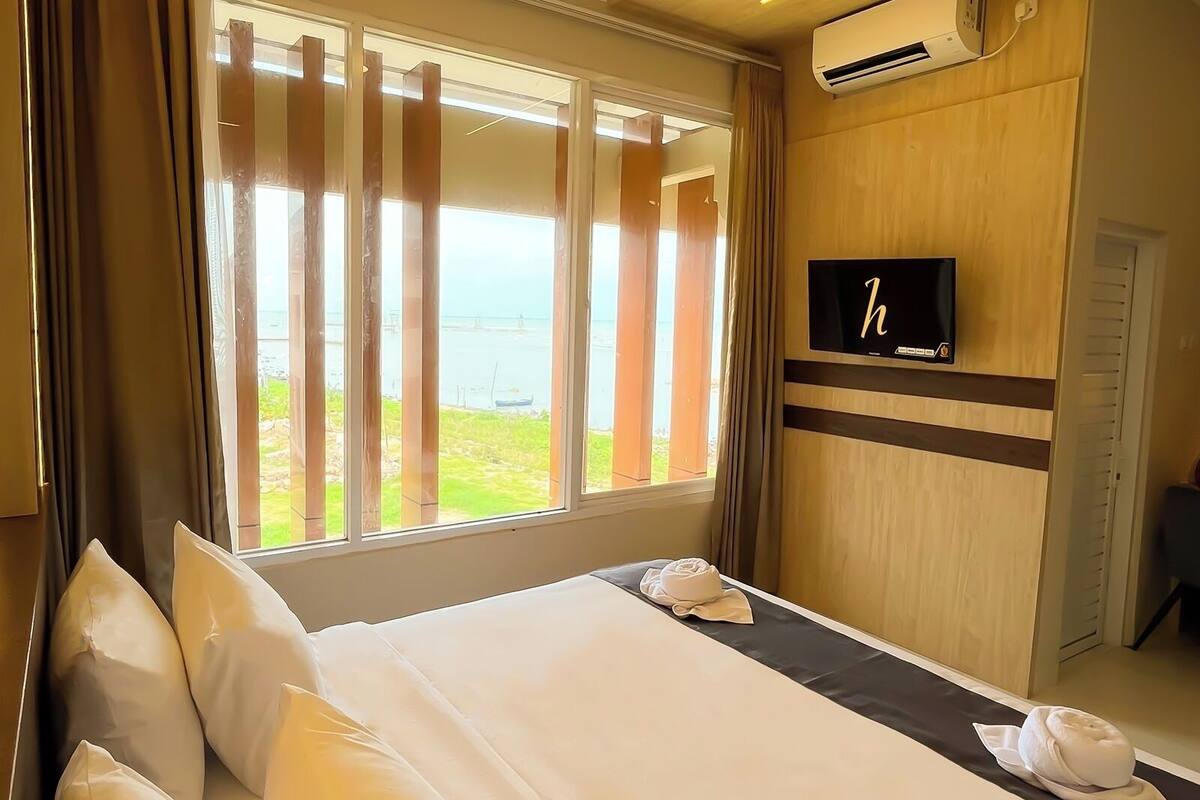 Een hotelkamer met een groot bed, een aan de muur bevestigde televisie en uitzicht op de zee.
