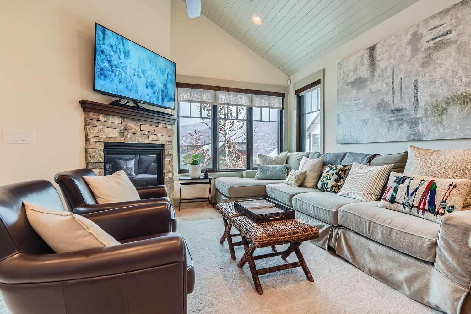 A living room with a stone fireplace, leather chairs, a grey sofa, and a large painting on the wall.
