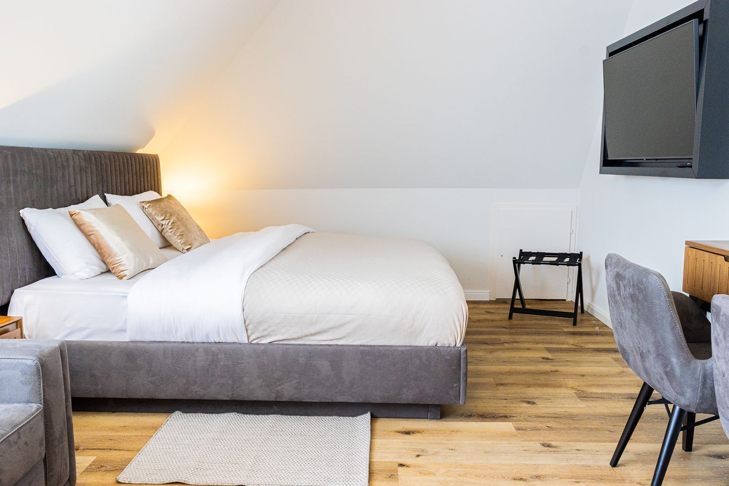 A modern bedroom with a bed, a grey sofa, a small table, and a television mounted on the wall.