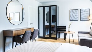 A modern hotel room with a bed, a desk, two chairs, a sofa, a small table, and a TV.