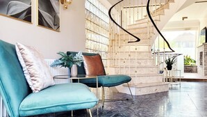 A modern interior with a curved staircase, teal upholstered chairs, and a marble floor.