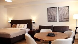 Habitación de hotel con cama, escritorio, dos sillas, una mesa redonda y dos lámparas fijadas a la pared.