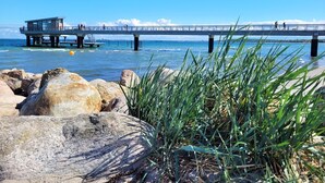 Un muelle que se adentra en el agua con una plataforma panorámica y un pequeño edificio, rodeado de rocas y hierba.