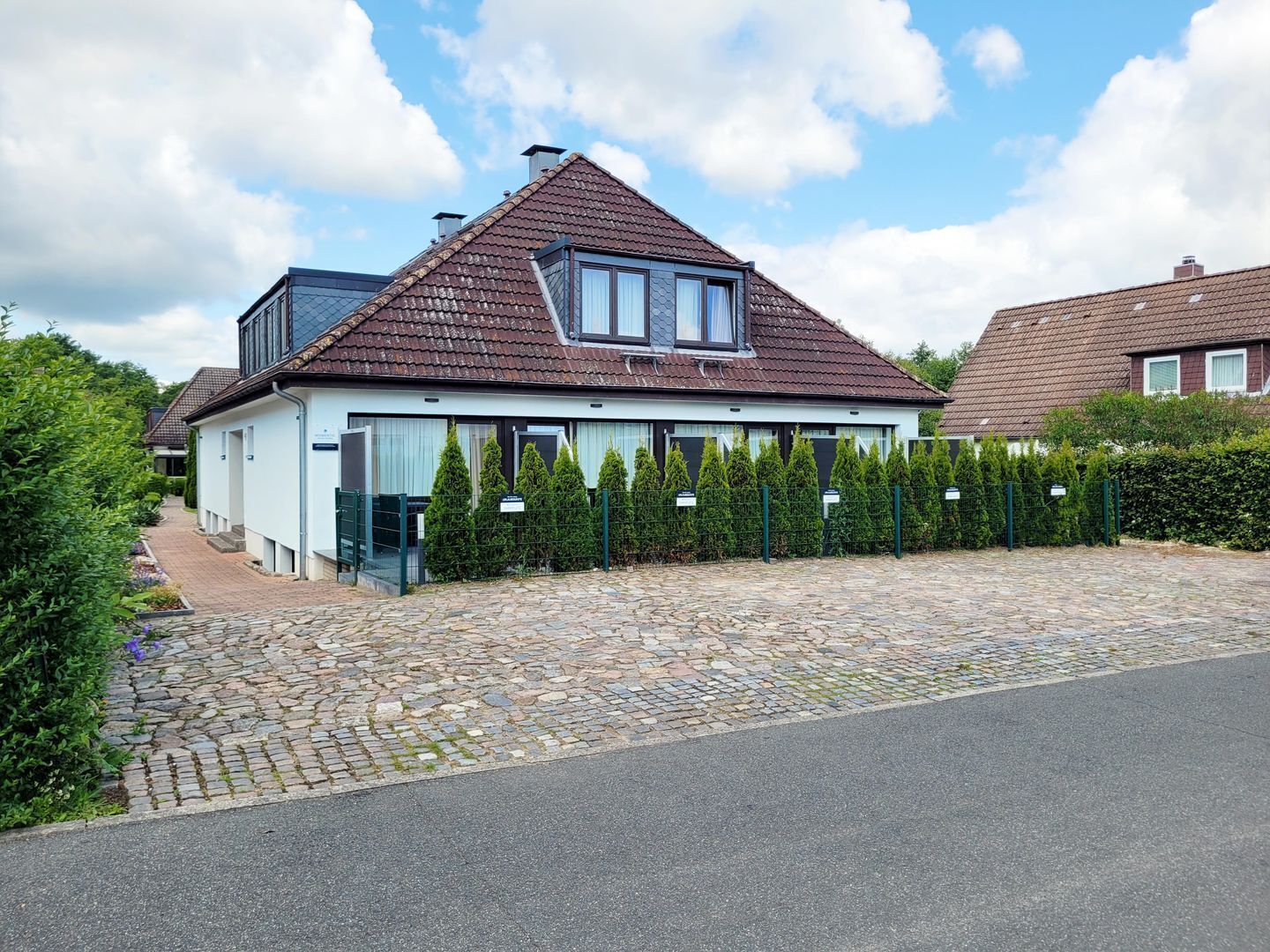 A modern house with a sloped roof, a paved driveway, and a well-maintained hedge.