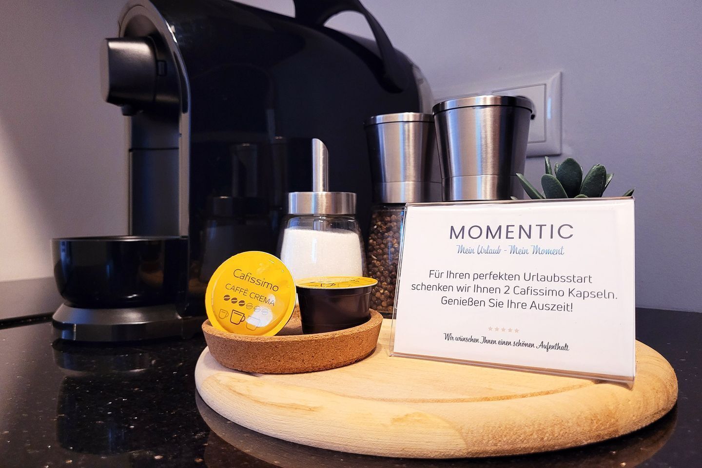 Una estación de café con una cafetera, un cartel que dice 'MOMENTIC' y dos cápsulas de café.