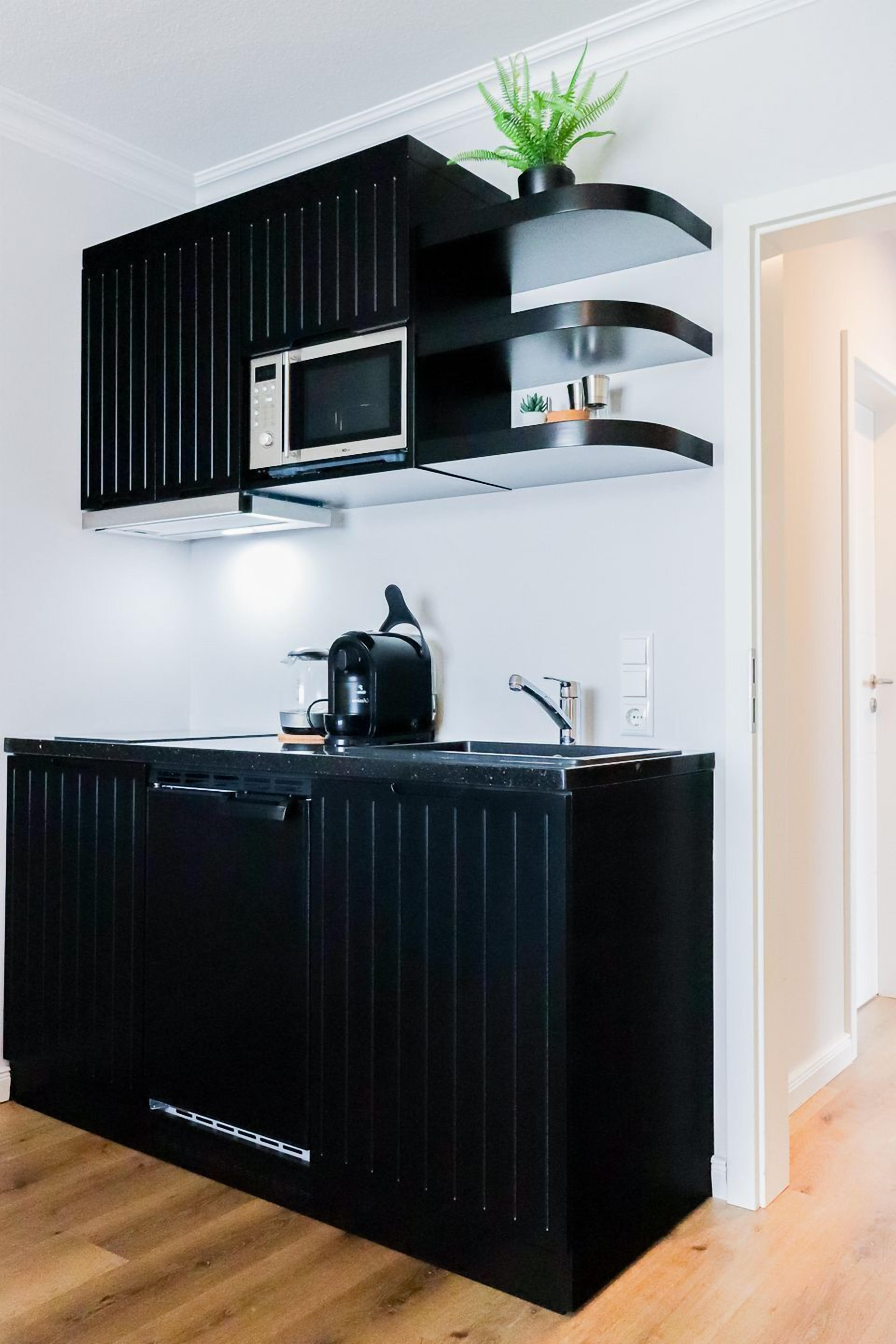 A compact kitchen with a microwave, kettle, and black cabinetry.