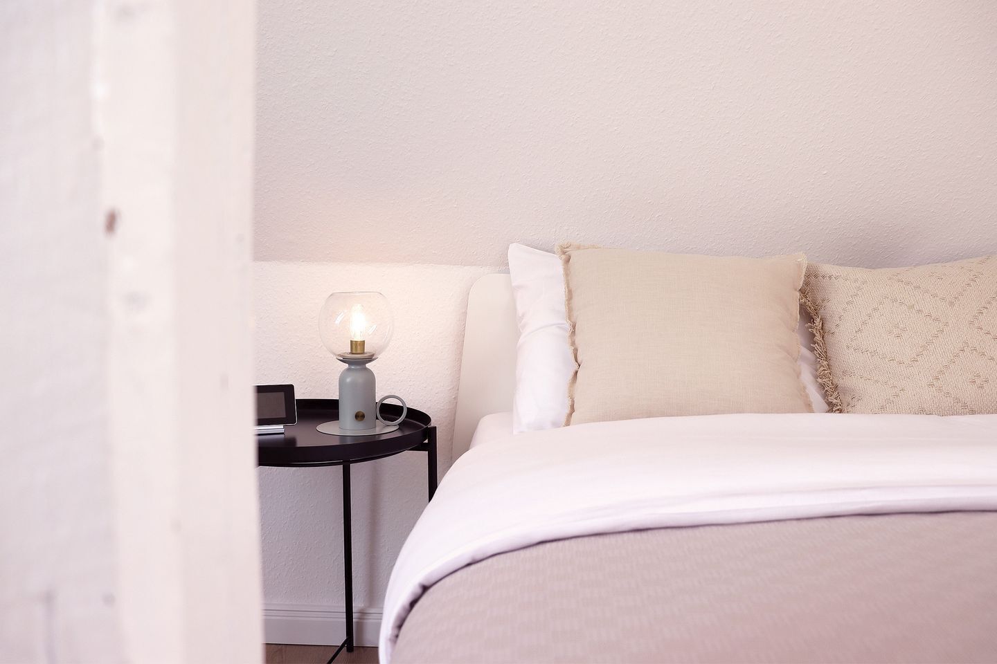 Une chambre à coucher avec un lit, une table de chevet avec une lampe et un mur blanc.