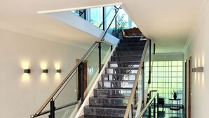 Ein modernes Interieur mit einer Marmortreppe, Glasgeländern und Blick ins Freie durch große Fenster.