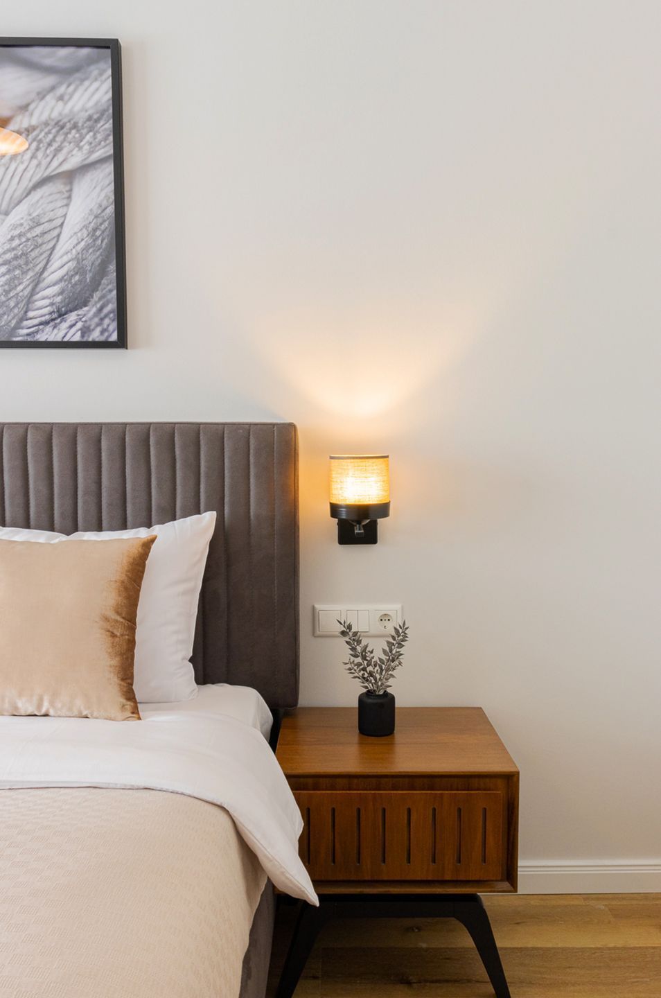 Un lit avec une tête de lit, une table de chevet avec une lampe et une prise de courant fixée au mur.
