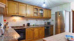 A kitchen with wooden cabinets, a stainless steel refrigerator, a microwave, and a granite countertop. - GuestReady - Breathtaking seaview in Caniço (Caniço)