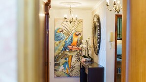 A hallway with a large tropical bird painting, a chandelier, and a mirror. - GuestReady - Breathtaking seaview in Caniço (Caniço)