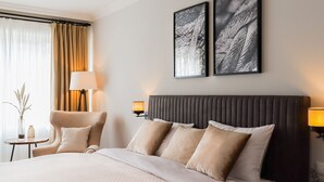 A hotel room with a large bed, two bedside lamps, a chair, a small table, and two framed pictures on the wall. - Modern vacation apartment with sun terrace & garden view - close to the beach and high (Scharbeutz)