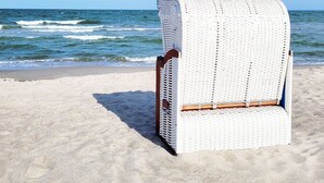 Ein Liegestuhl am sandigen Strand mit dem Meer im Hintergrund.