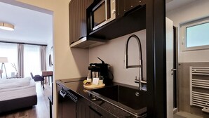 Eine kompakte Küche mit dunklen Schränken, einer eingebauten Mikrowelle, einer Kaffeemaschine und einem modernen Wasserhahn.