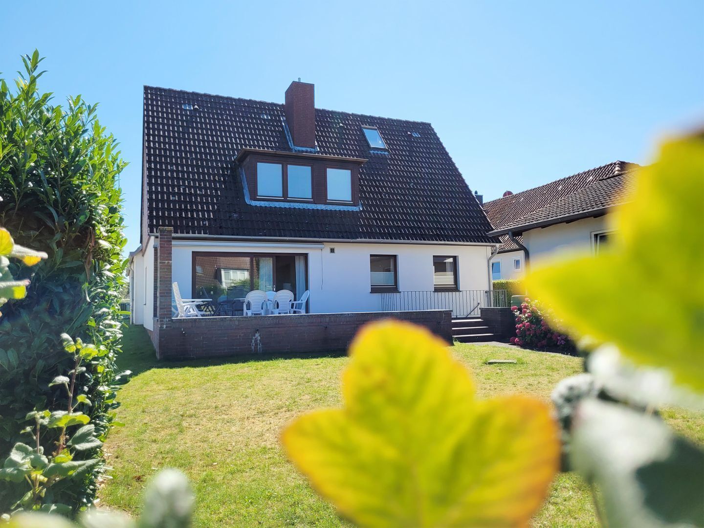 Ein zweistöckiges Haus mit einem geneigten Dach, einem Schornstein und einem Balkon mit Gartenmöbeln.