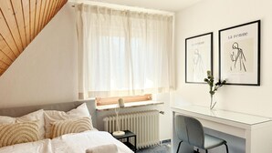 A modern hotel room with a bed, a desk, and two framed artworks on the wall.