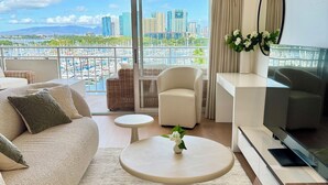 A modern living room with a sofa, two chairs, a coffee table, and a TV. The room has large windows with a city view. - 2 Queen Beds Beachfront Home (Car Available) (Honolulu)
