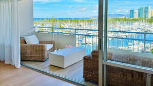 A balcony with wicker furniture, a glass door, and a view of a marina with boats and buildings. - 2 Queen Beds Beachfront Home (Car Available) (Honolulu)