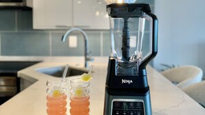 Una cucina con un frullatore moderno, un bicchiere di succo d'arancia e fiori decorativi sul bancone.