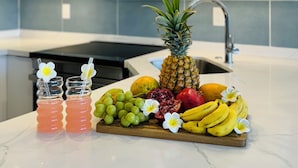 Una cucina moderna con mobili bianchi, un forno a microonde in acciaio inossidabile e un vassoio di frutta sul piano di lavoro.