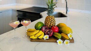 A modern kitchen with a marble countertop, a hanging light fixture, and a fruit and drink display. - White Sand Beach House (Car Available) (Honolulu)