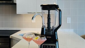 A kitchen with a black Ninja blender, two martini glasses with flowers, and hanging pendant lights. - White Sand Beach House (Car Available) (Honolulu)