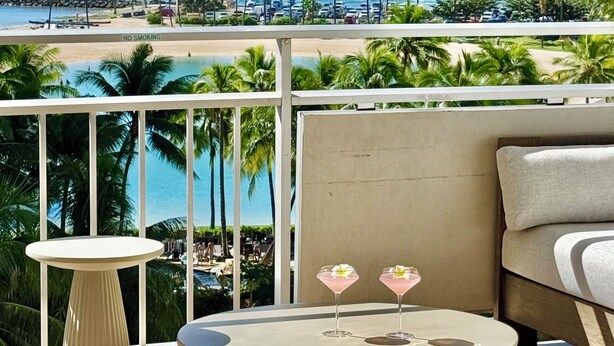A balcony with a view of the ocean, a round table with two drinks, and a sofa. - White Sand Beach House (Car Available) (Honolulu)