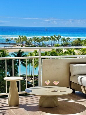 Un balcon avec vue sur l’océan, une table ronde avec deux boissons et un canapé.