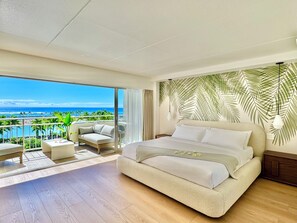 Une chambre dotée d’un grand lit, d’un balcon offrant une vue sur l’océan et d’un décor mural représentant des feuilles tropicales.