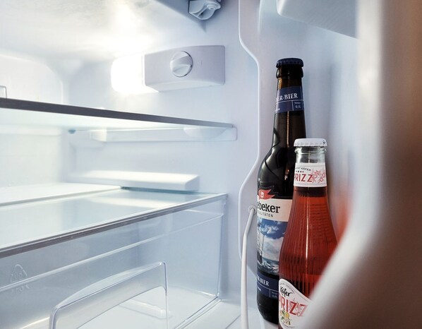 Un refrigerador abierto con dos botellas de cerveza y una botella de Prizz.