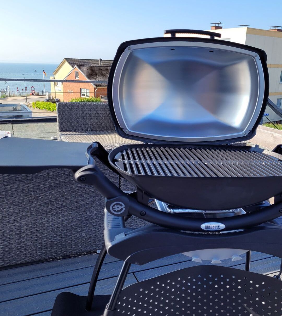 A grill on an outdoor table with a view of a building and the sea.