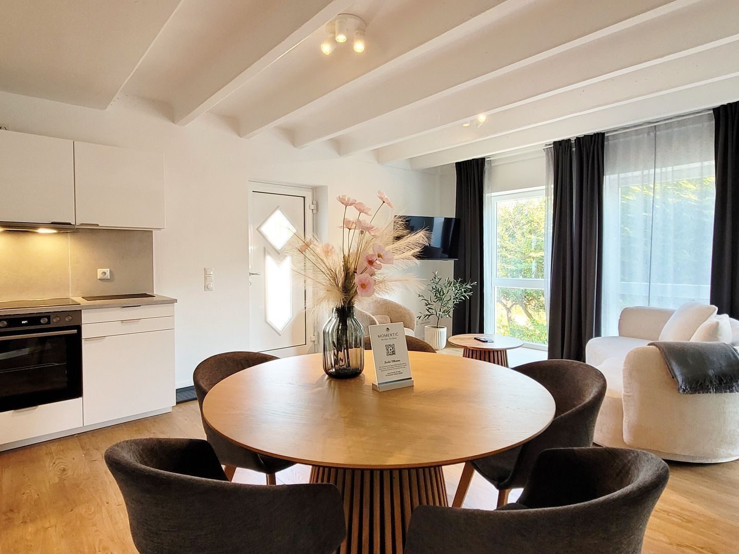 Eine moderne Küche mit weißen Schränken, einem eingebauten Backofen und einem Essbereich mit einem runden Holztisch und dunklen Stühlen.