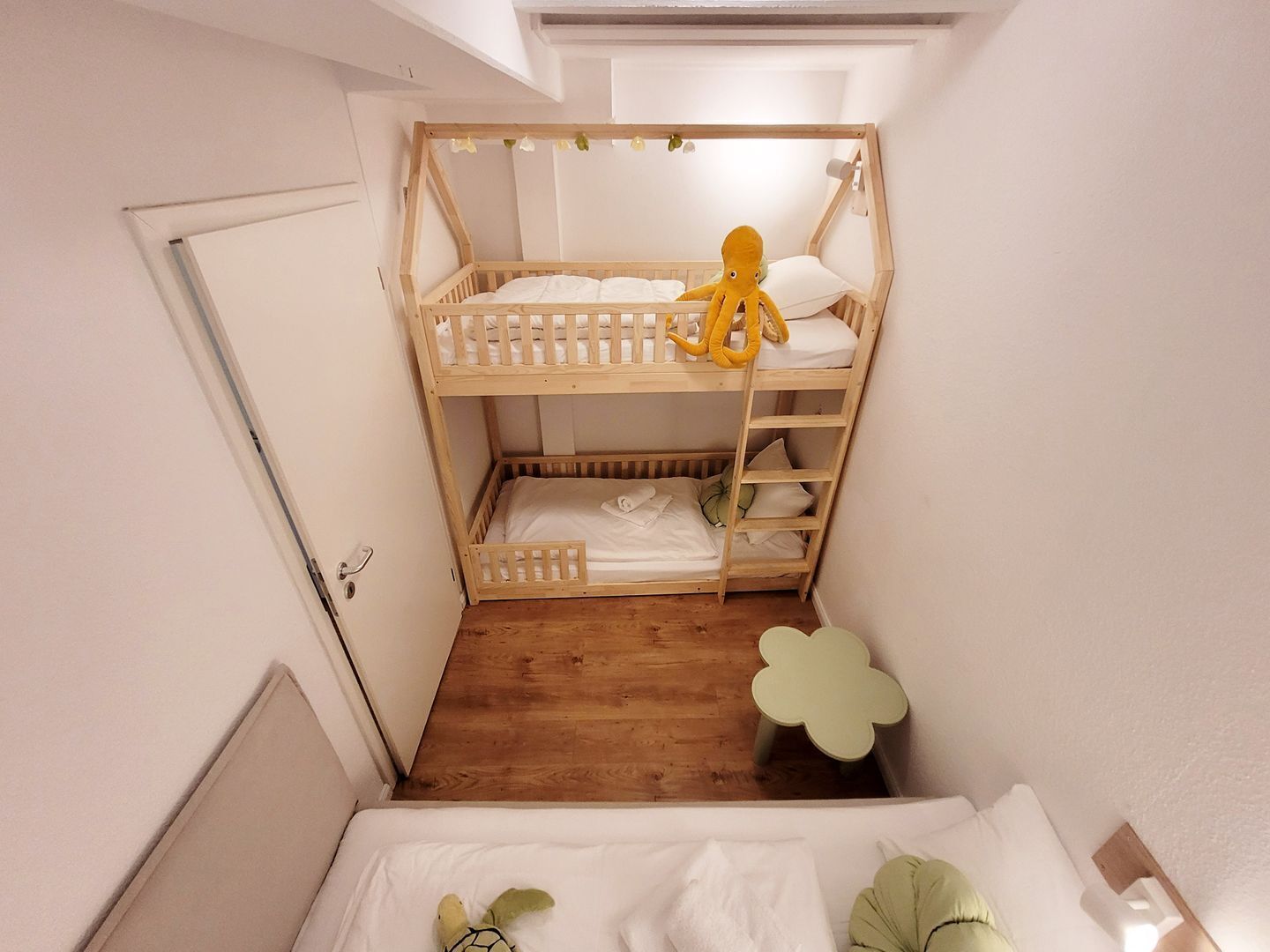 Une chambre avec un lit superposé, une échelle en bois, une petite table et une porte.