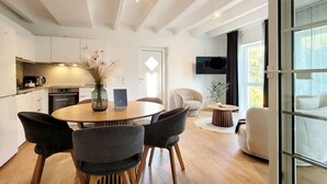 A modern kitchen with a dining area, a TV mounted on the wall, and a large window.