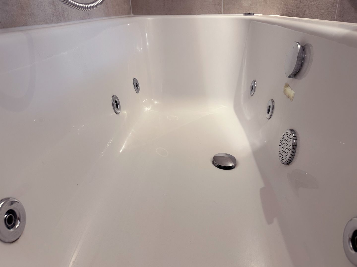 Eine weiße Badewanne mit Ablass, Wasserhahn und Duschkopf.