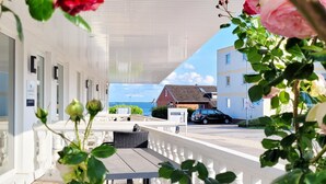 Een balkon met uitzicht op zee, een wit gebouw en een geparkeerde auto.
