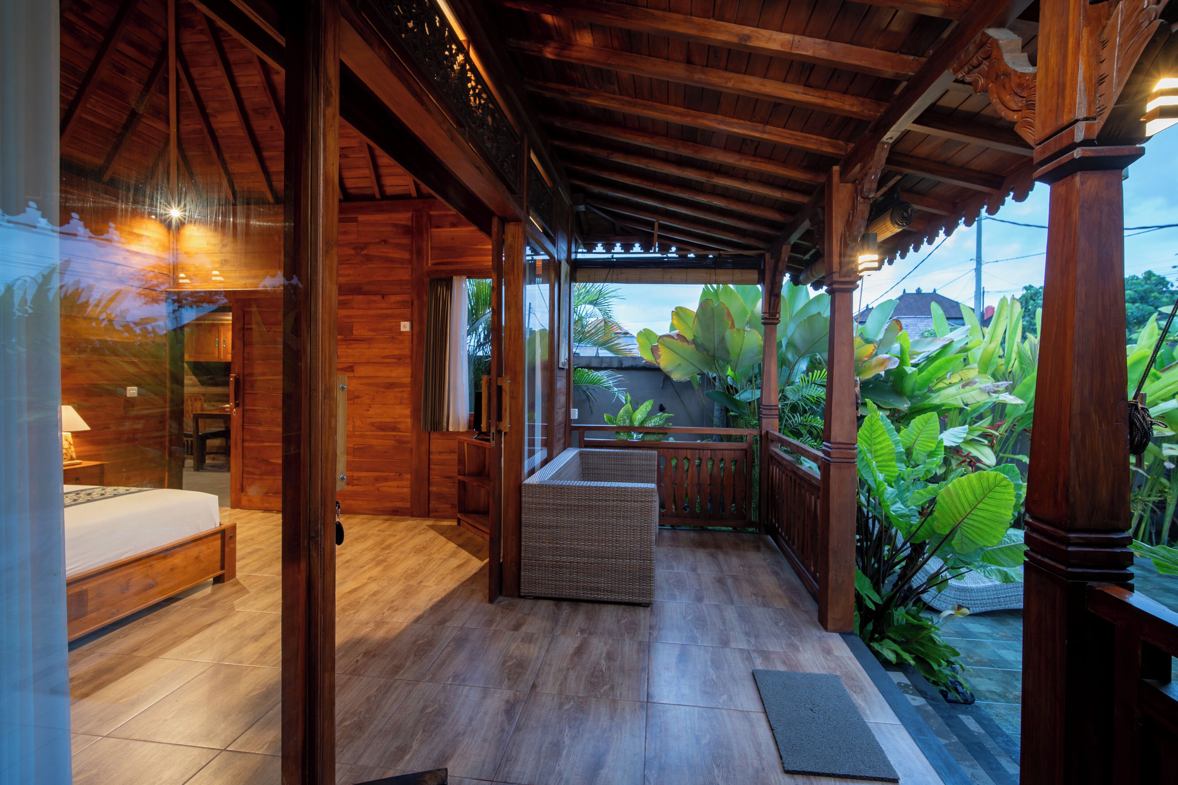 A wooden room with a bed, a wicker chair, and a view of lush greenery outside.