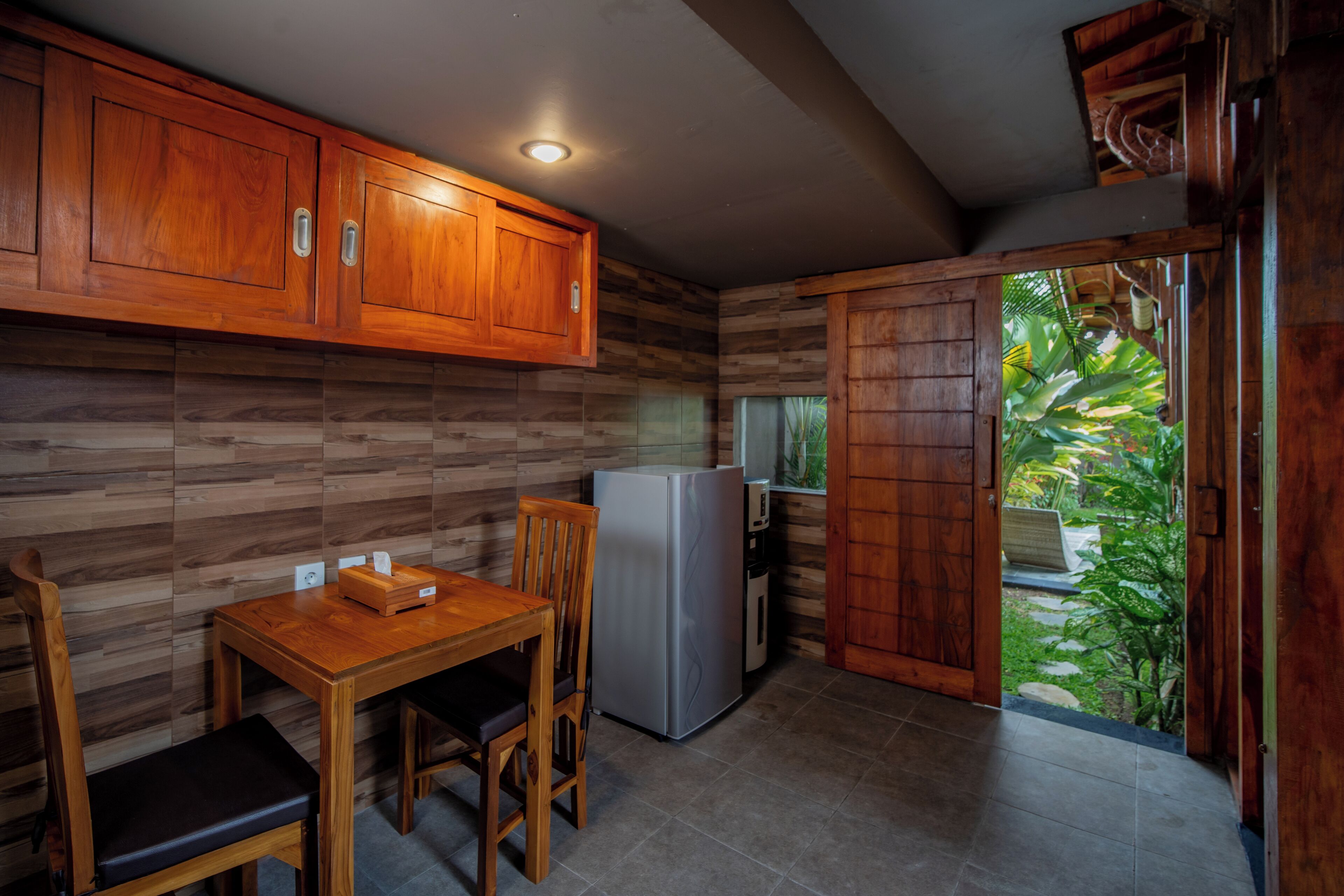 A compact kitchen with wooden cabinets, a refrigerator, and a dining table with chairs.