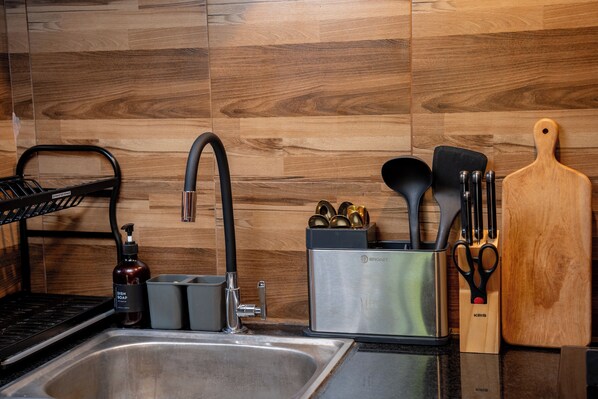 A kitchen with a stainless steel sink, a black faucet, and wooden backsplash. - Pertiwi Uma Sari (Ubud)