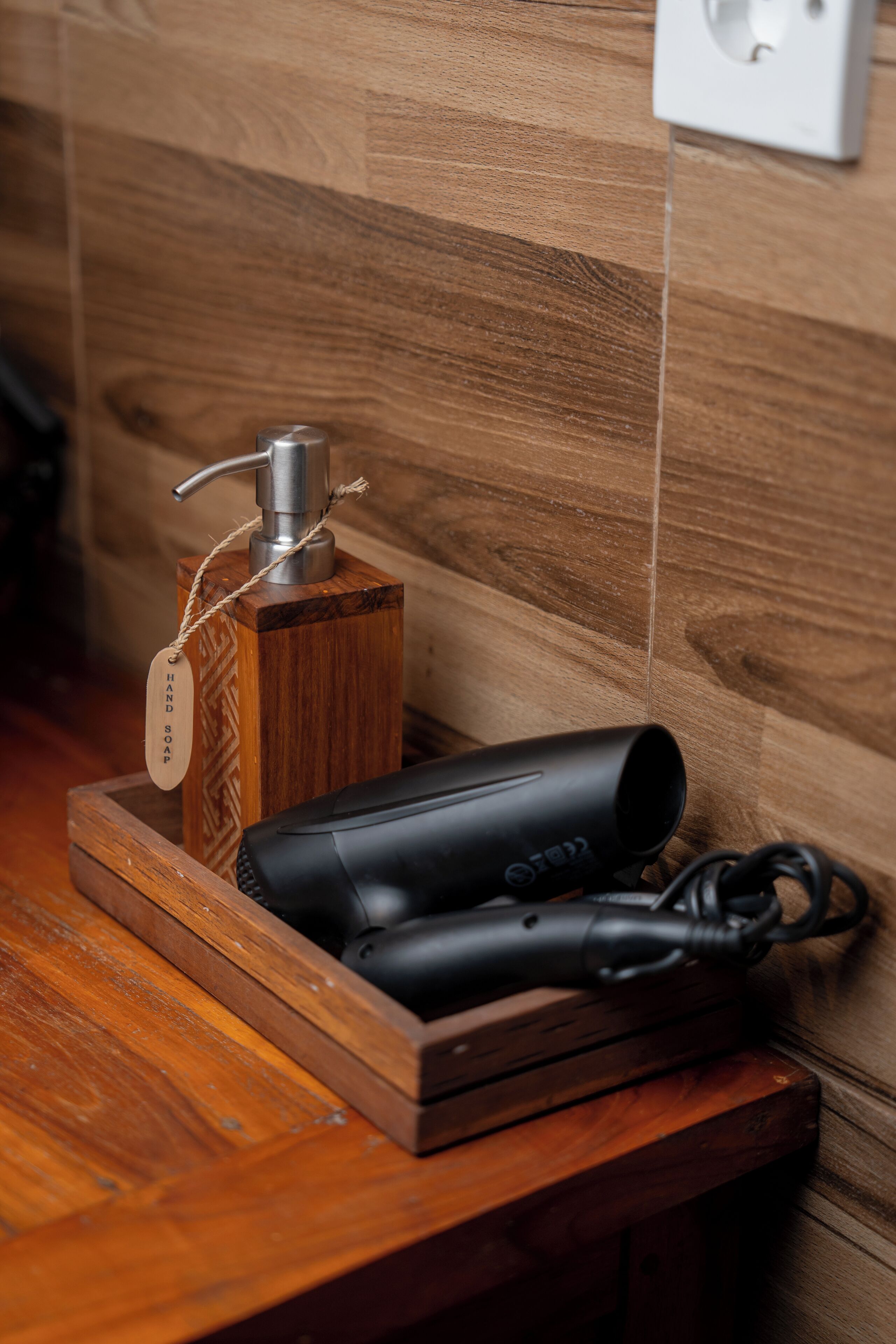 Una bandeja de madera con un secador negro y un dispensador de jabón de madera sobre una mesa de madera.