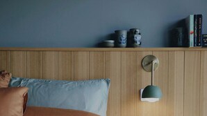 Ein Schlafzimmer mit einem hölzernen Kopfende, einem Nachttisch, einer Lampe und einem Regal mit Büchern und Dekoration.