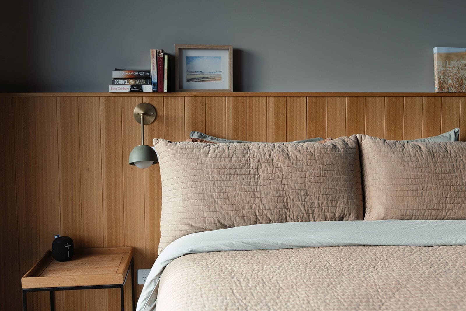 A bedroom with a wooden headboard, a bedside table with a lamp, and a bed with a quilted cover.