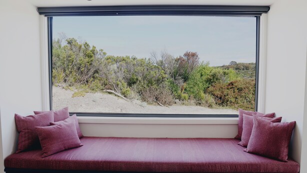 Ein Zimmer mit einem großen Fenster, einer dunkelblauen Bank mit roten Kissen und Blick auf eine natürliche Landschaft.