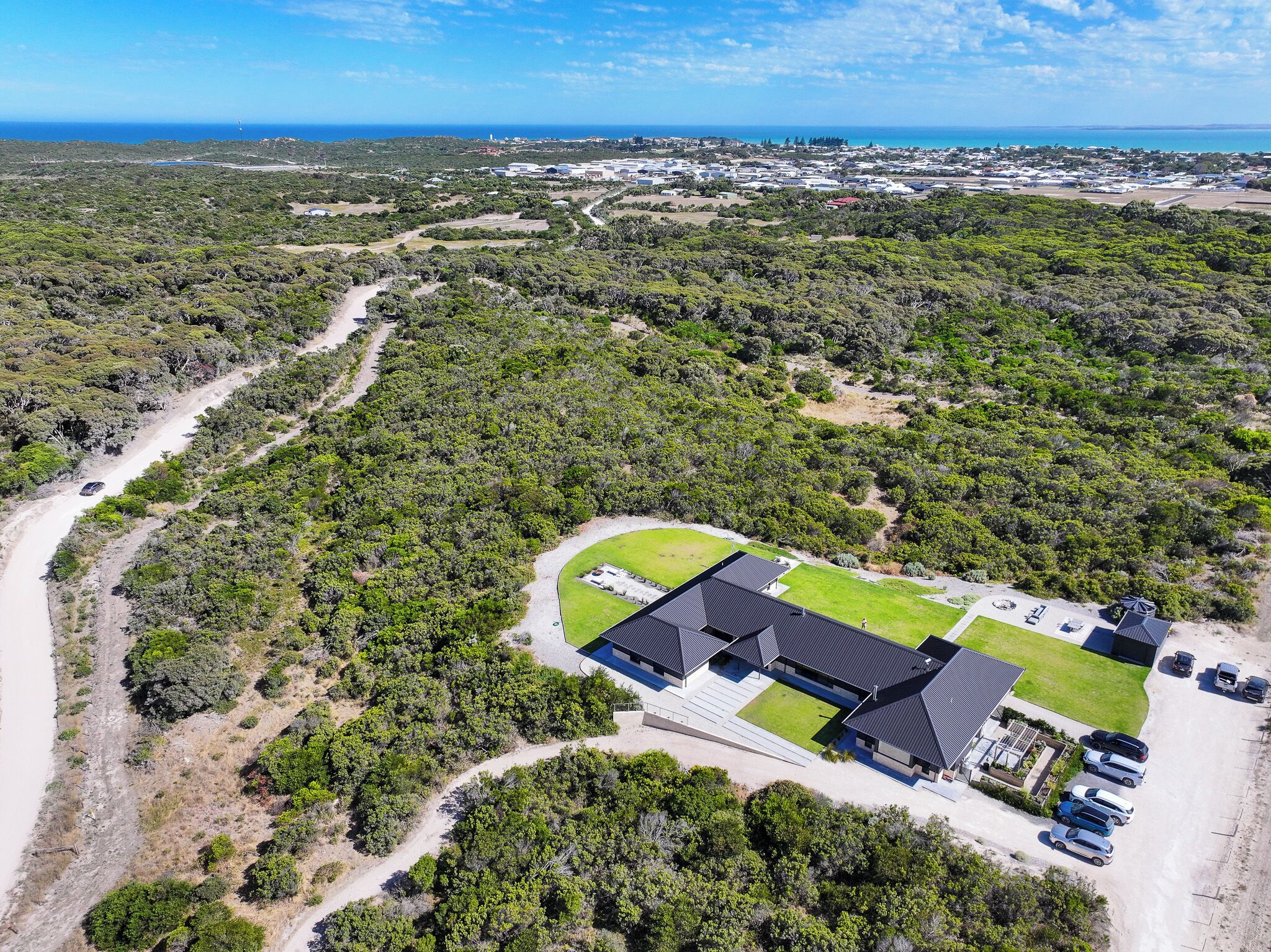 An aerial view of a property with a large building, parking area, and surrounding greenery.