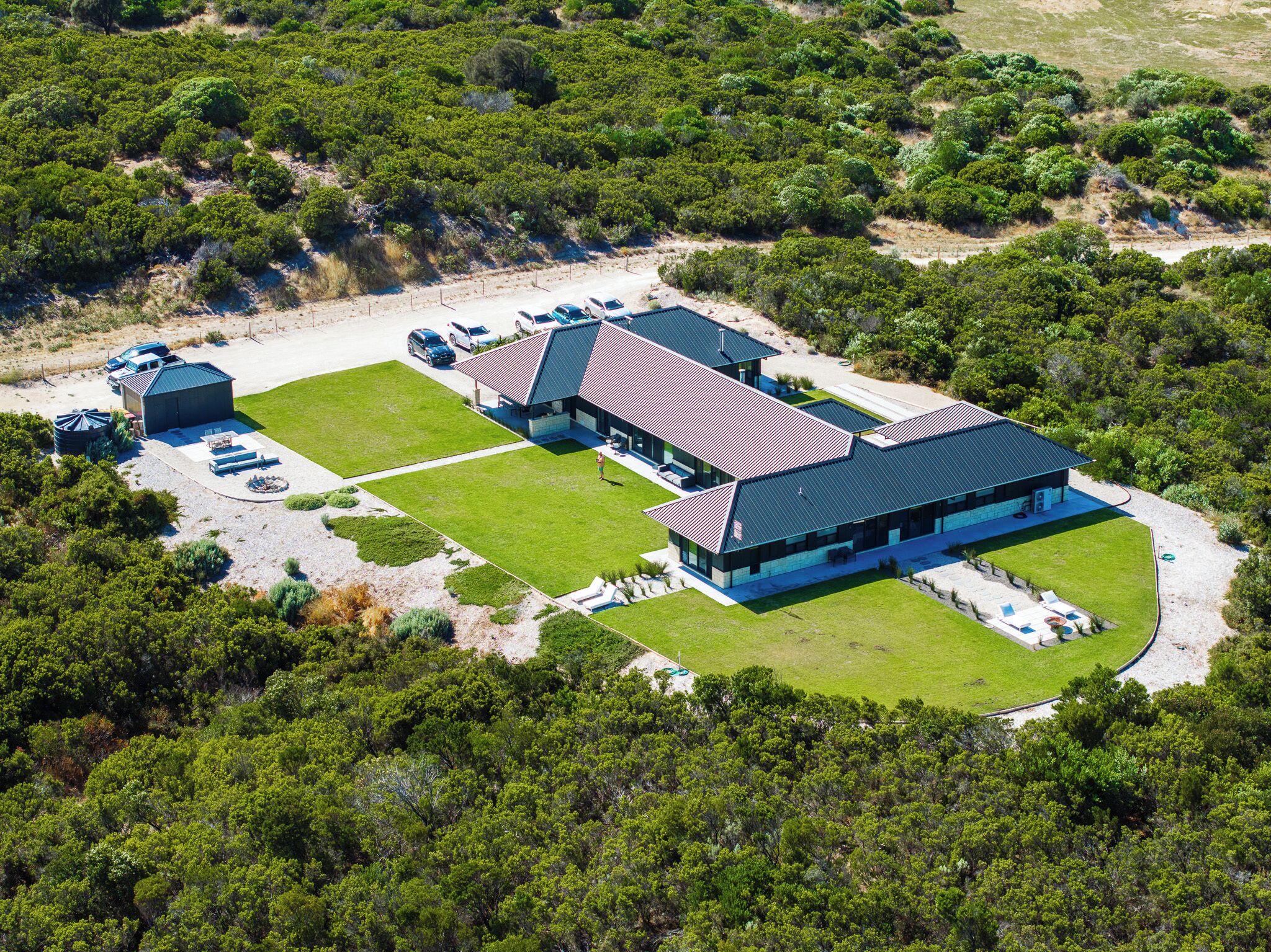 A modern building with a flat roof, surrounded by a well-maintained lawn and a parking area with several cars.
