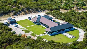A modern building with a flat roof, surrounded by a well-maintained lawn and a parking area with several cars.