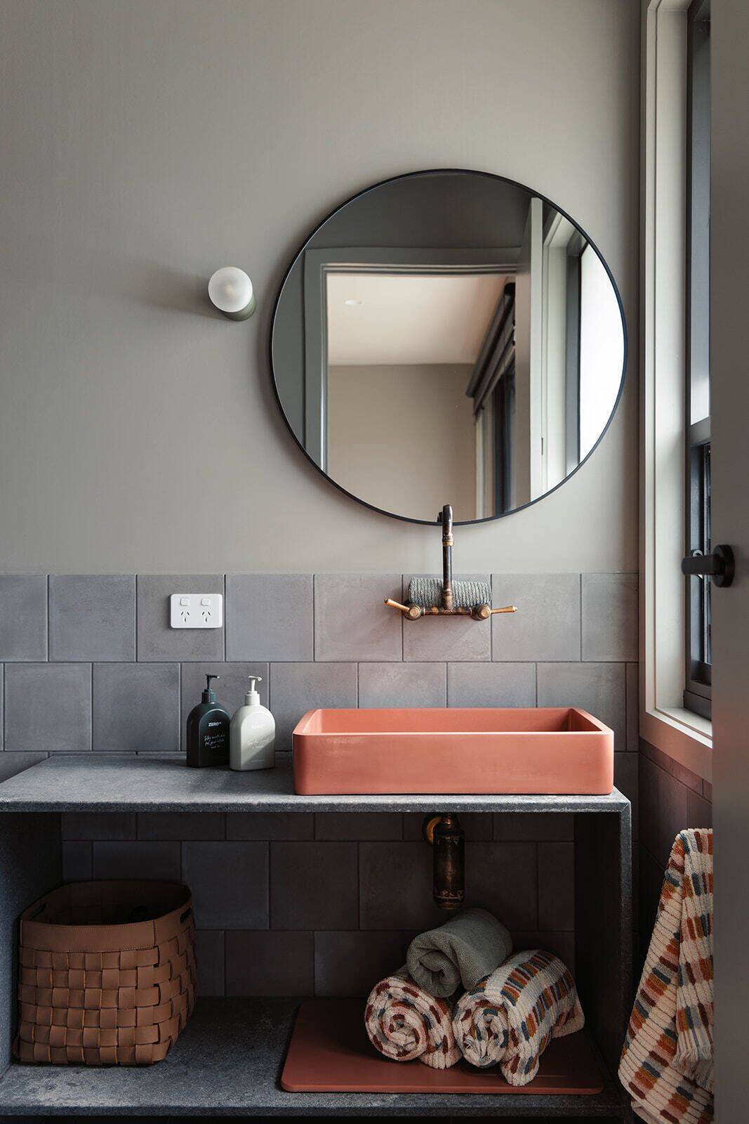 Un baño con un espejo redondo, un lavabo rectangular y un perchero para toallas.