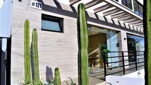 A building with a light-colored facade, a sign reading "#121", and a modern entrance with a glass door. - Intimate & Bright Studio w/ Rooftop Pool in the Art District San Jose Del Cabo (San José del Cabo)