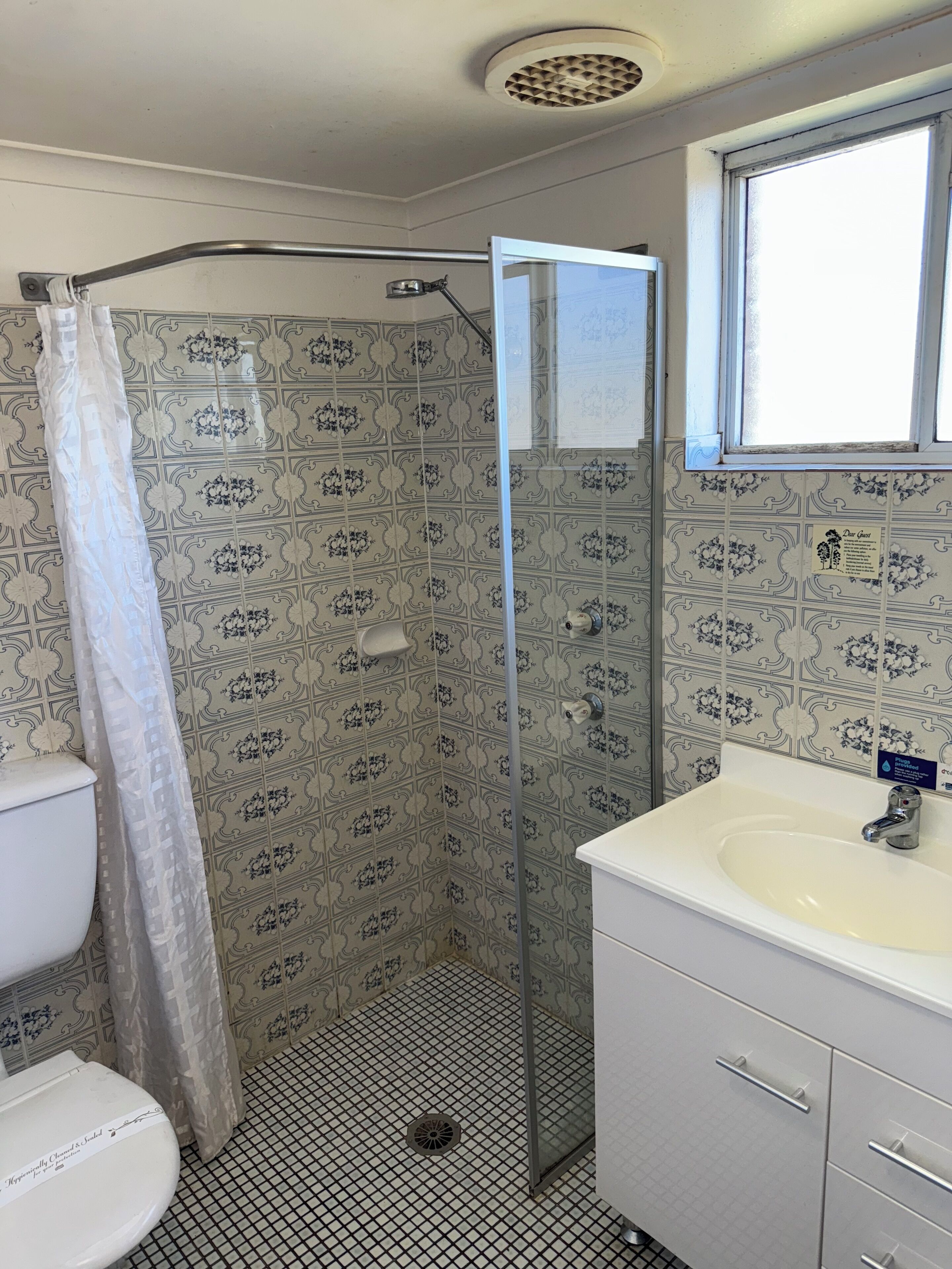A bathroom with a shower, toilet, sink, and patterned tiles.
